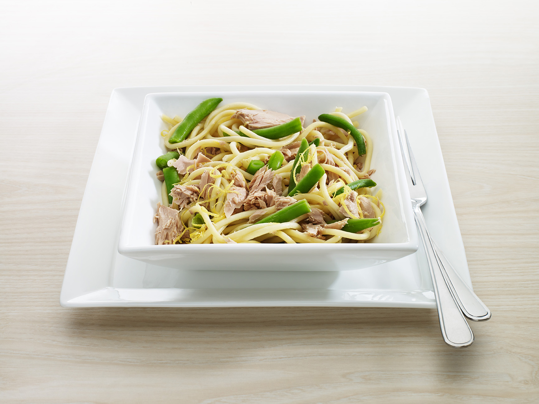 Spaghetti with tuna, cheese and green beans in a white bowl